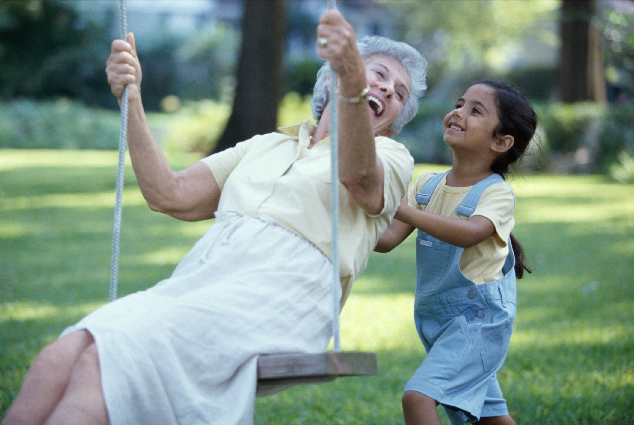 A granddaughter pushing her grandmother on a swing