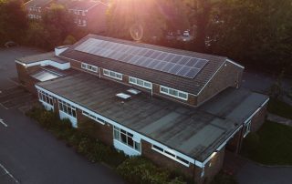 Photograph of Banstead Community Hall with a low sun glowing over the image, shot with a drone