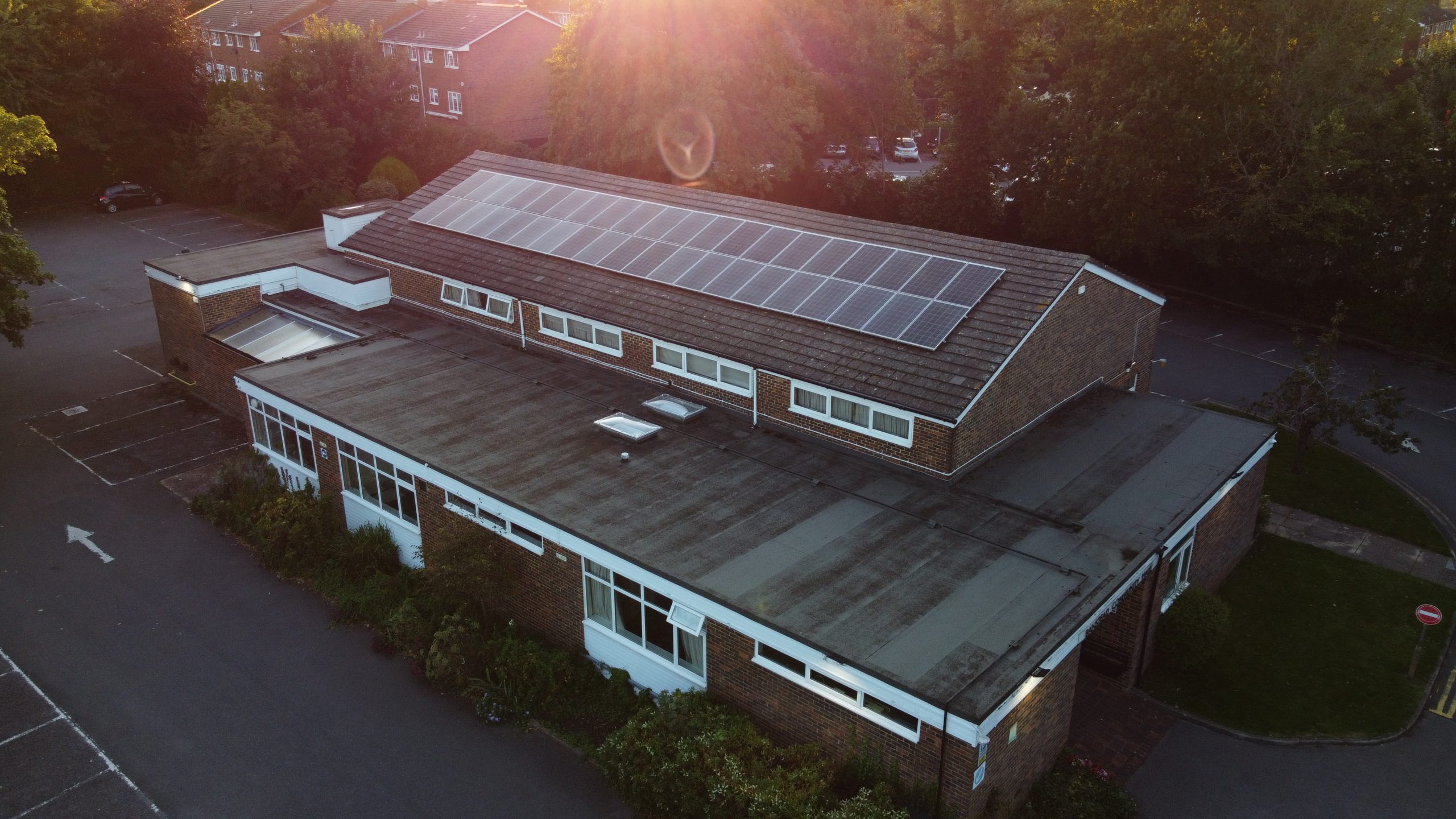 Photograph of Banstead Community Hall with a low sun glowing over the image, shot with a drone